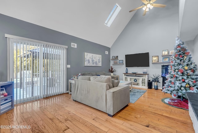 living room featuring ceiling fan, light hardwood / wood-style floors, high vaulted ceiling, and a skylight