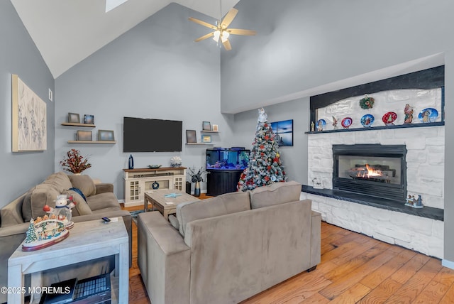 living room with a fireplace, ceiling fan, light hardwood / wood-style flooring, and high vaulted ceiling