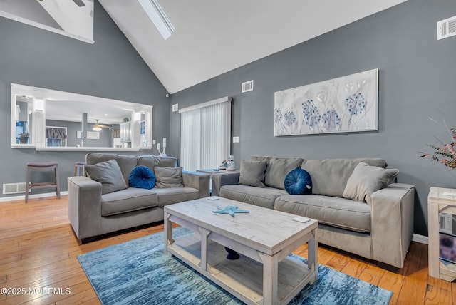 living room featuring a skylight, high vaulted ceiling, ceiling fan, and light hardwood / wood-style floors