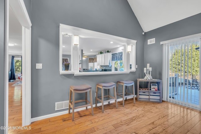 kitchen with kitchen peninsula, light hardwood / wood-style flooring, a breakfast bar area, white cabinets, and lofted ceiling