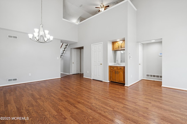 unfurnished living room featuring ceiling fan with notable chandelier, a high ceiling, and wood-type flooring