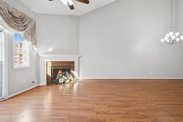 unfurnished living room with hardwood / wood-style flooring, a tile fireplace, and ceiling fan with notable chandelier