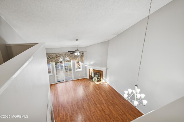 unfurnished living room featuring a tiled fireplace, ceiling fan with notable chandelier, a textured ceiling, and hardwood / wood-style floors