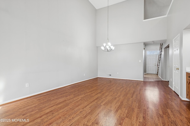 unfurnished living room with high vaulted ceiling, hardwood / wood-style floors, and a chandelier