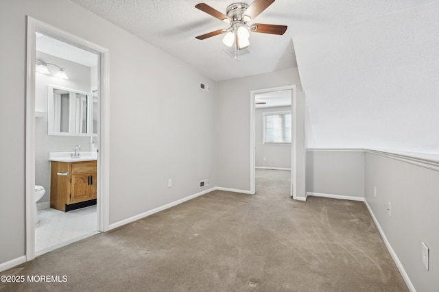 unfurnished bedroom featuring a textured ceiling, light carpet, sink, ceiling fan, and ensuite bathroom