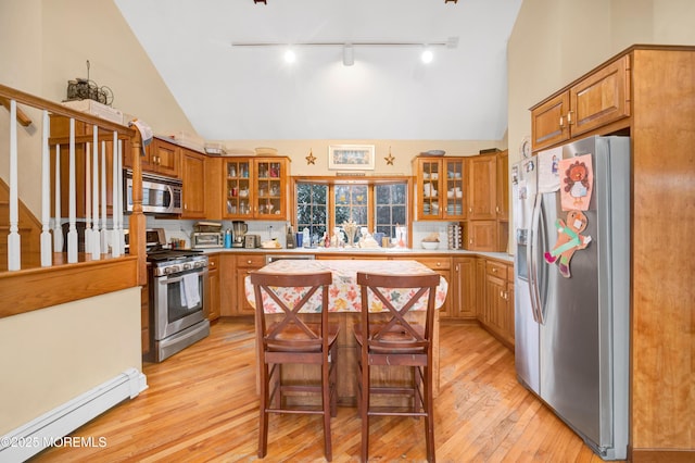 kitchen featuring appliances with stainless steel finishes, a kitchen island, a baseboard heating unit, light hardwood / wood-style floors, and a breakfast bar area