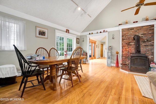 dining space with light hardwood / wood-style floors, ceiling fan, a wood stove, lofted ceiling, and french doors