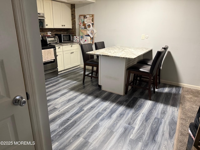 kitchen featuring decorative backsplash, electric range, white cabinetry, and a breakfast bar area