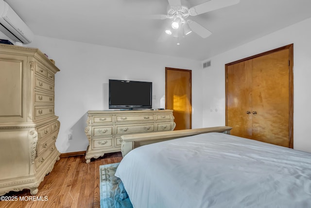 bedroom featuring ceiling fan, light wood-type flooring, and a wall mounted air conditioner