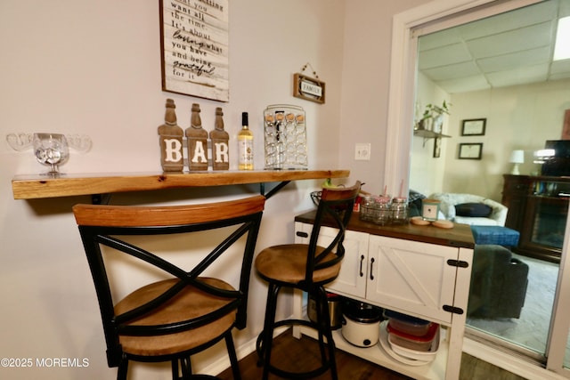 bar with a paneled ceiling, dark hardwood / wood-style flooring, and white cabinetry