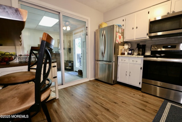 kitchen with decorative backsplash, stainless steel appliances, ceiling fan, light hardwood / wood-style flooring, and white cabinetry