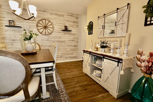 dining area with a chandelier, a barn door, wood walls, and dark wood-type flooring