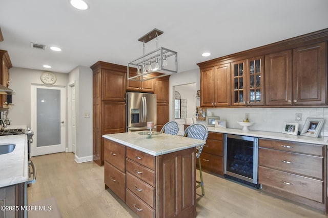 kitchen with backsplash, a center island with sink, stainless steel refrigerator with ice dispenser, hanging light fixtures, and light wood-type flooring