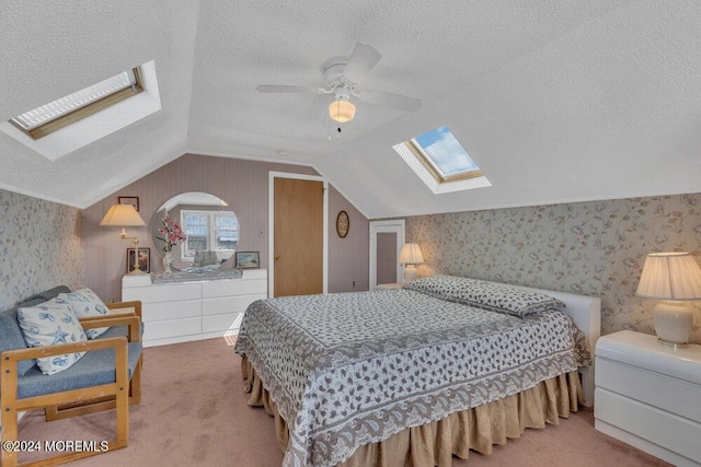 carpeted bedroom with a textured ceiling, lofted ceiling with skylight, and ceiling fan