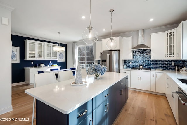 kitchen with pendant lighting, wall chimney range hood, appliances with stainless steel finishes, white cabinetry, and a center island