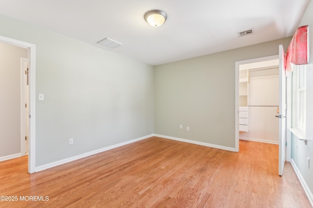 unfurnished bedroom with baseboards, a spacious closet, visible vents, and light wood-style floors