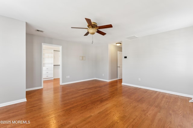 empty room featuring baseboards, ceiling fan, visible vents, and wood finished floors