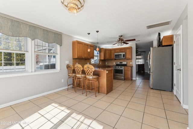 kitchen with light tile patterned floors, a peninsula, visible vents, appliances with stainless steel finishes, and brown cabinetry