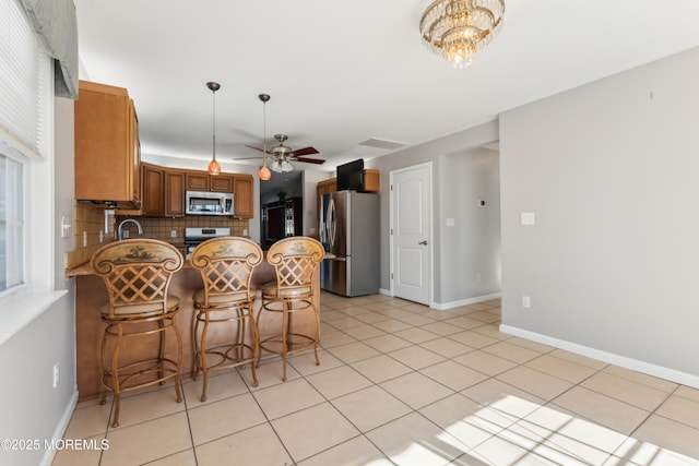 kitchen featuring decorative backsplash, appliances with stainless steel finishes, brown cabinets, a peninsula, and light tile patterned flooring