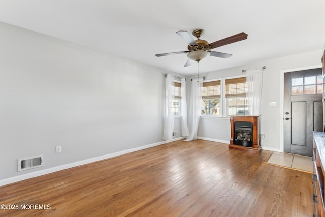 unfurnished living room with ceiling fan, a fireplace, wood finished floors, visible vents, and baseboards