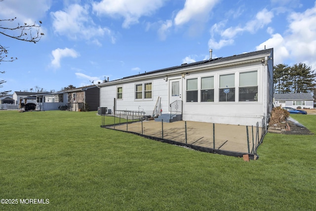 back of property with solar panels, cooling unit, and a lawn