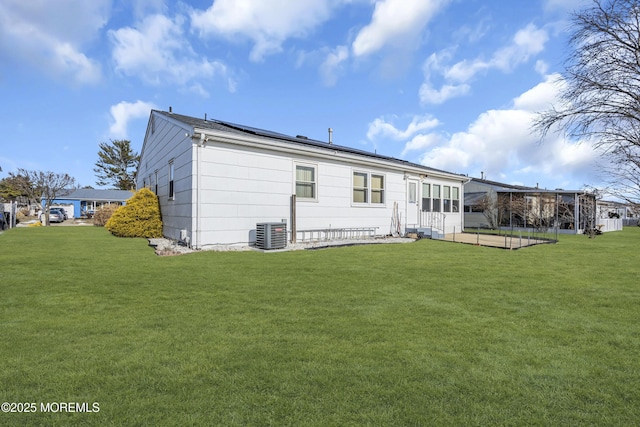 rear view of property featuring solar panels, a yard, and central AC