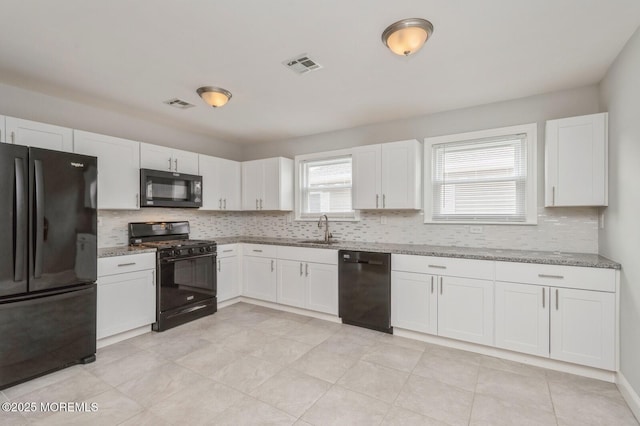 kitchen with decorative backsplash, light stone counters, sink, black appliances, and white cabinets