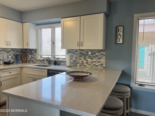 kitchen featuring sink, white cabinetry, light stone counters, backsplash, and a breakfast bar