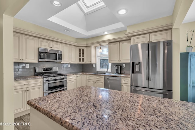 kitchen with cream cabinetry, appliances with stainless steel finishes, backsplash, and light stone counters