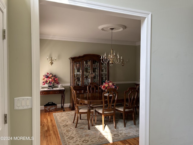 dining area with wood-type flooring, an inviting chandelier, and crown molding