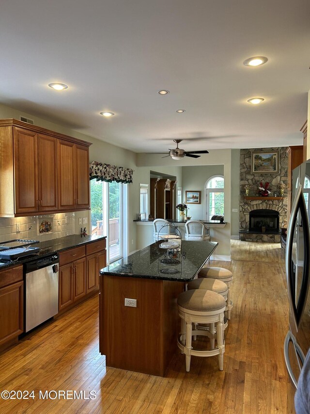 kitchen featuring a stone fireplace, ceiling fan, light wood-type flooring, a kitchen island, and stainless steel appliances