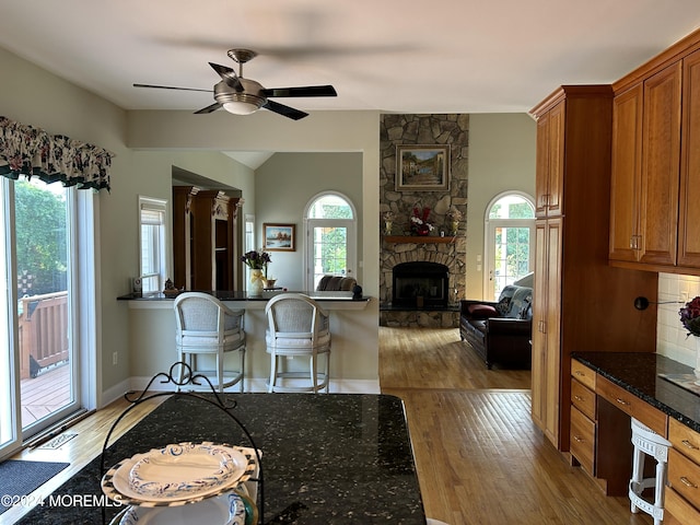 kitchen featuring a healthy amount of sunlight, dark stone countertops, light hardwood / wood-style floors, decorative backsplash, and a fireplace