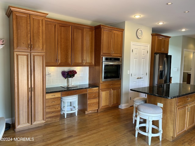 kitchen with tasteful backsplash, dark stone countertops, wood-type flooring, a kitchen island, and appliances with stainless steel finishes