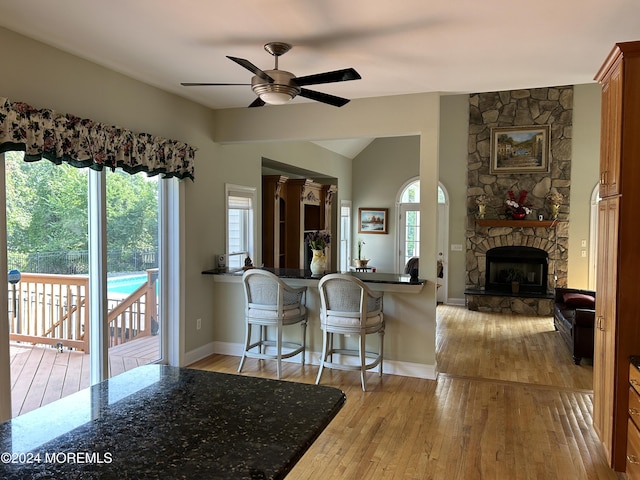 kitchen featuring kitchen peninsula, a kitchen breakfast bar, ceiling fan, light hardwood / wood-style flooring, and a fireplace