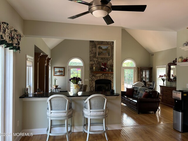 kitchen with vaulted ceiling, hardwood / wood-style flooring, ceiling fan, a fireplace, and kitchen peninsula