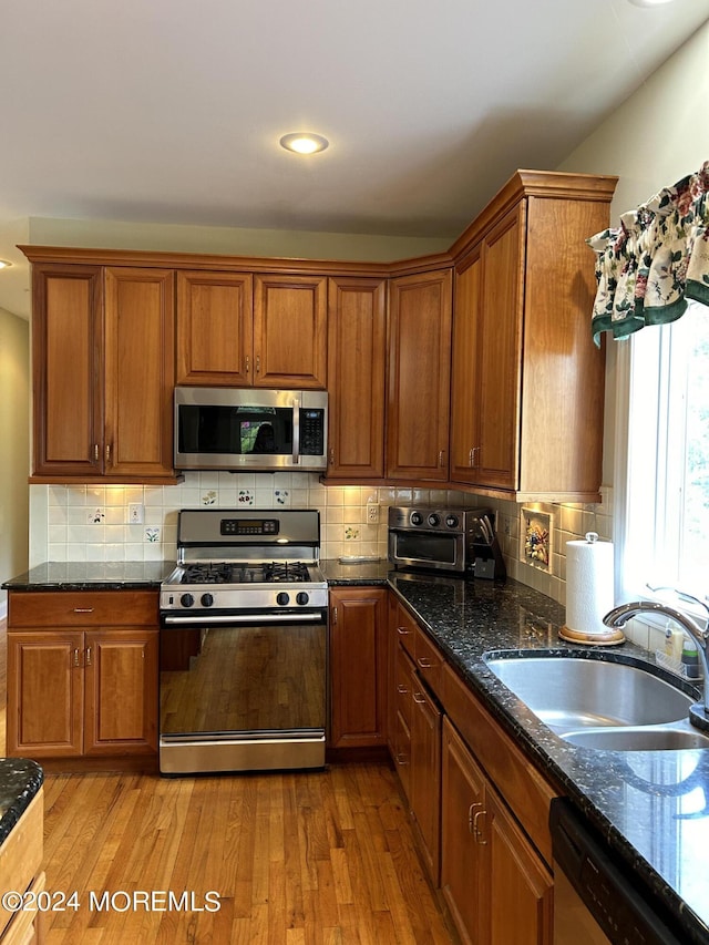 kitchen featuring sink, stainless steel appliances, dark stone countertops, light hardwood / wood-style floors, and decorative backsplash