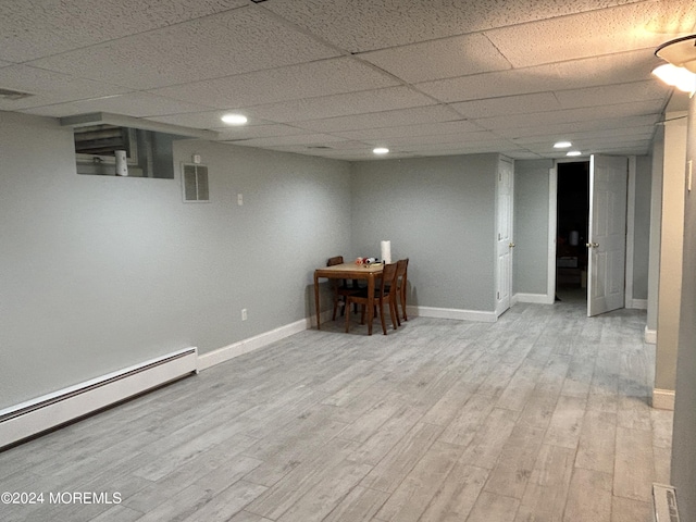 basement with a drop ceiling, light wood-type flooring, and a baseboard radiator