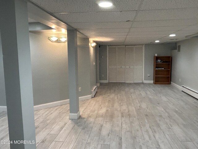 basement featuring a drop ceiling, light hardwood / wood-style flooring, and a baseboard heating unit