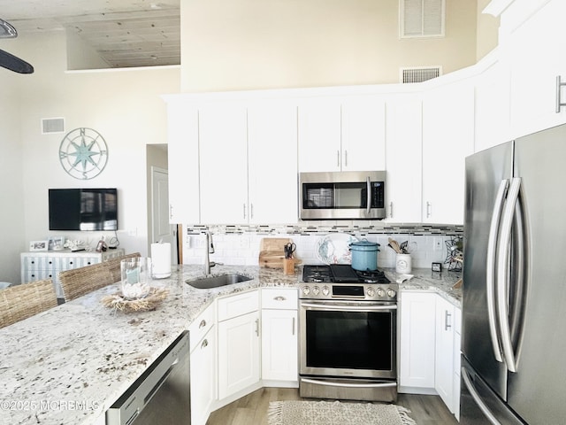 kitchen with stainless steel appliances, sink, white cabinets, light hardwood / wood-style flooring, and light stone countertops