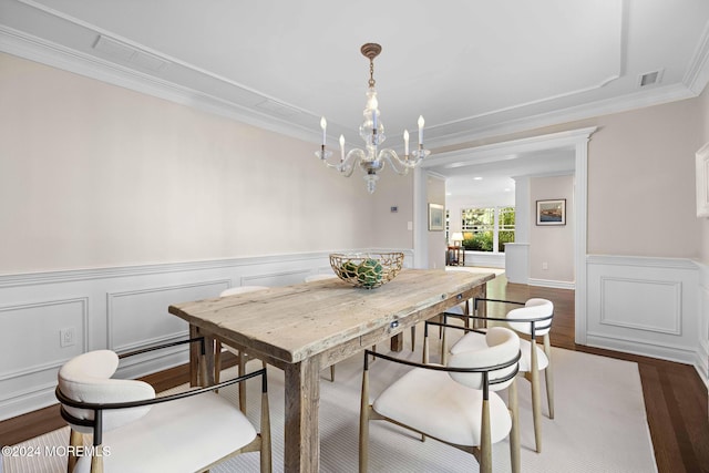 dining space with hardwood / wood-style flooring, ornamental molding, and an inviting chandelier