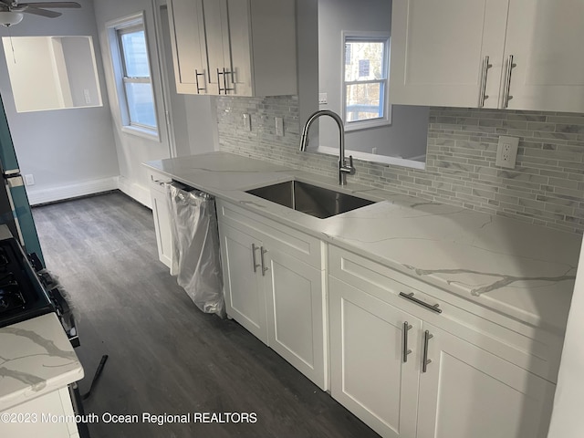 kitchen with light stone countertops, backsplash, stainless steel dishwasher, sink, and white cabinets