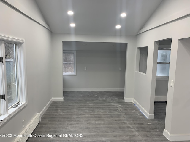 unfurnished room with baseboard heating, dark wood-type flooring, and lofted ceiling