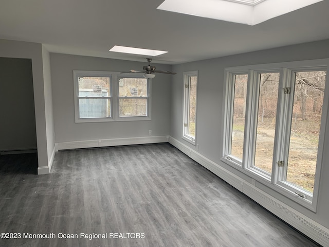 unfurnished room with hardwood / wood-style floors, ceiling fan, a baseboard heating unit, and vaulted ceiling with skylight