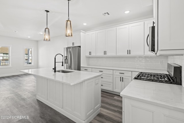 kitchen with white cabinets, appliances with stainless steel finishes, pendant lighting, and a kitchen island with sink