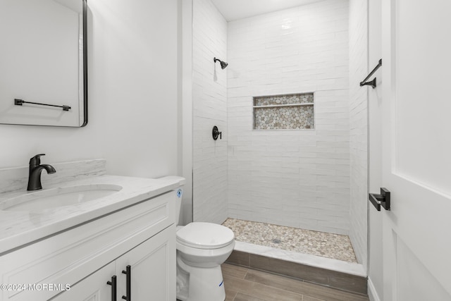 bathroom with toilet, tiled shower, and vanity