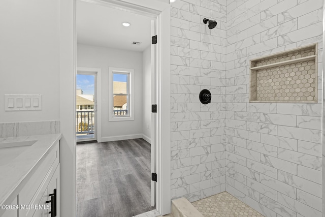 bathroom with hardwood / wood-style floors, a tile shower, and vanity