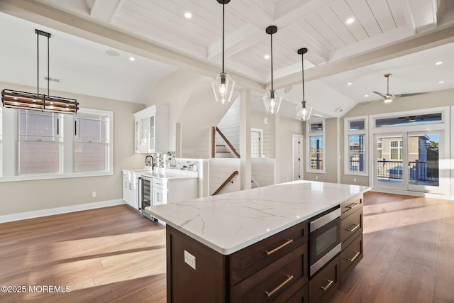 kitchen with ceiling fan with notable chandelier, pendant lighting, hardwood / wood-style flooring, beamed ceiling, and stainless steel microwave