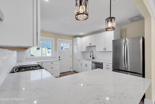 kitchen with appliances with stainless steel finishes, hanging light fixtures, light stone countertops, white cabinetry, and backsplash