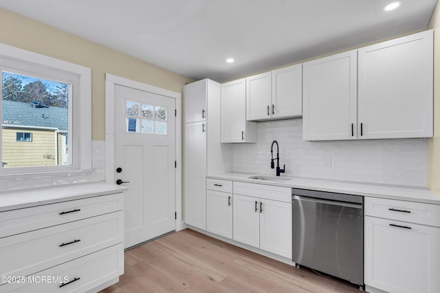 kitchen featuring sink, white cabinetry, light hardwood / wood-style flooring, stainless steel dishwasher, and backsplash