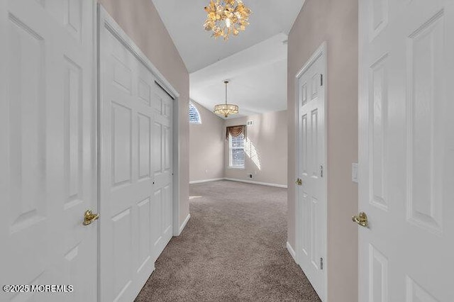 hallway with an inviting chandelier, vaulted ceiling, and carpet